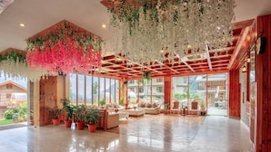 Un hall d’entrée spacieux avec un plafond en bois, de grandes fenêtres et un coin salon agrémenté de canapés et de plantes en pot.