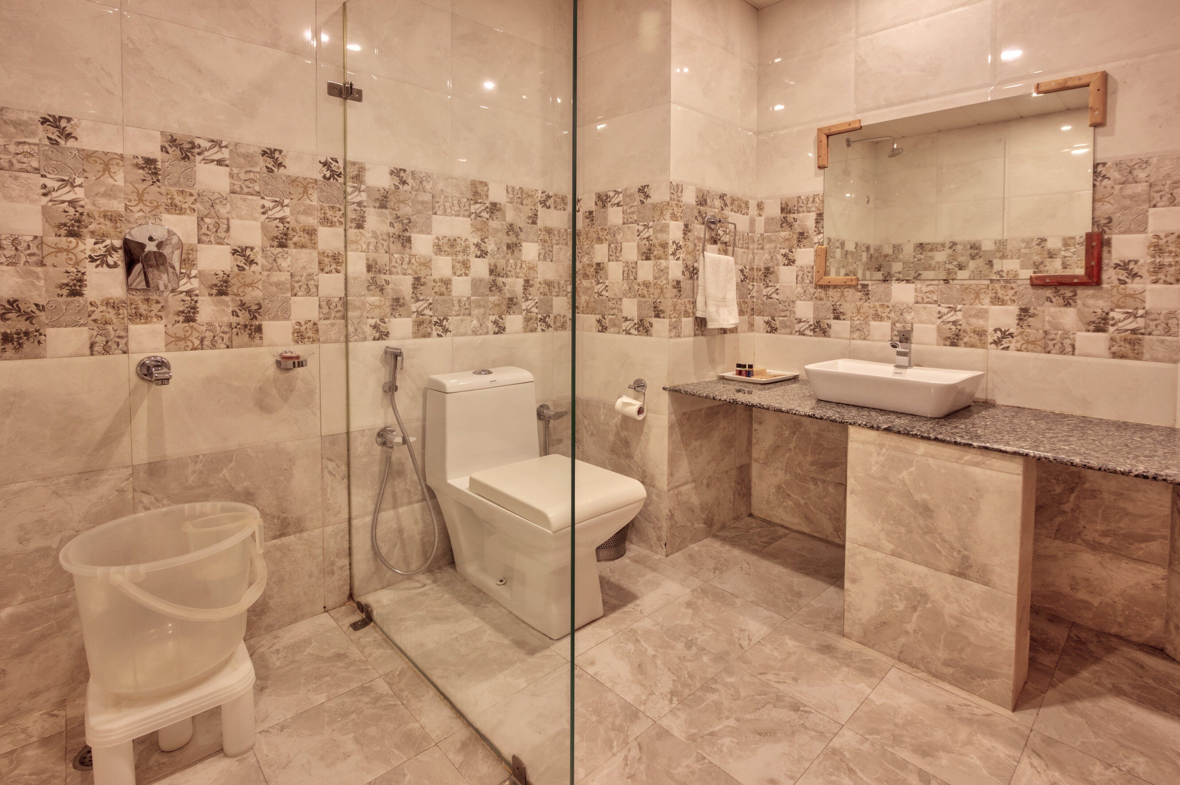 A modern bathroom with a glass-enclosed shower, a white toilet, and a marble-tiled vanity with a sink.