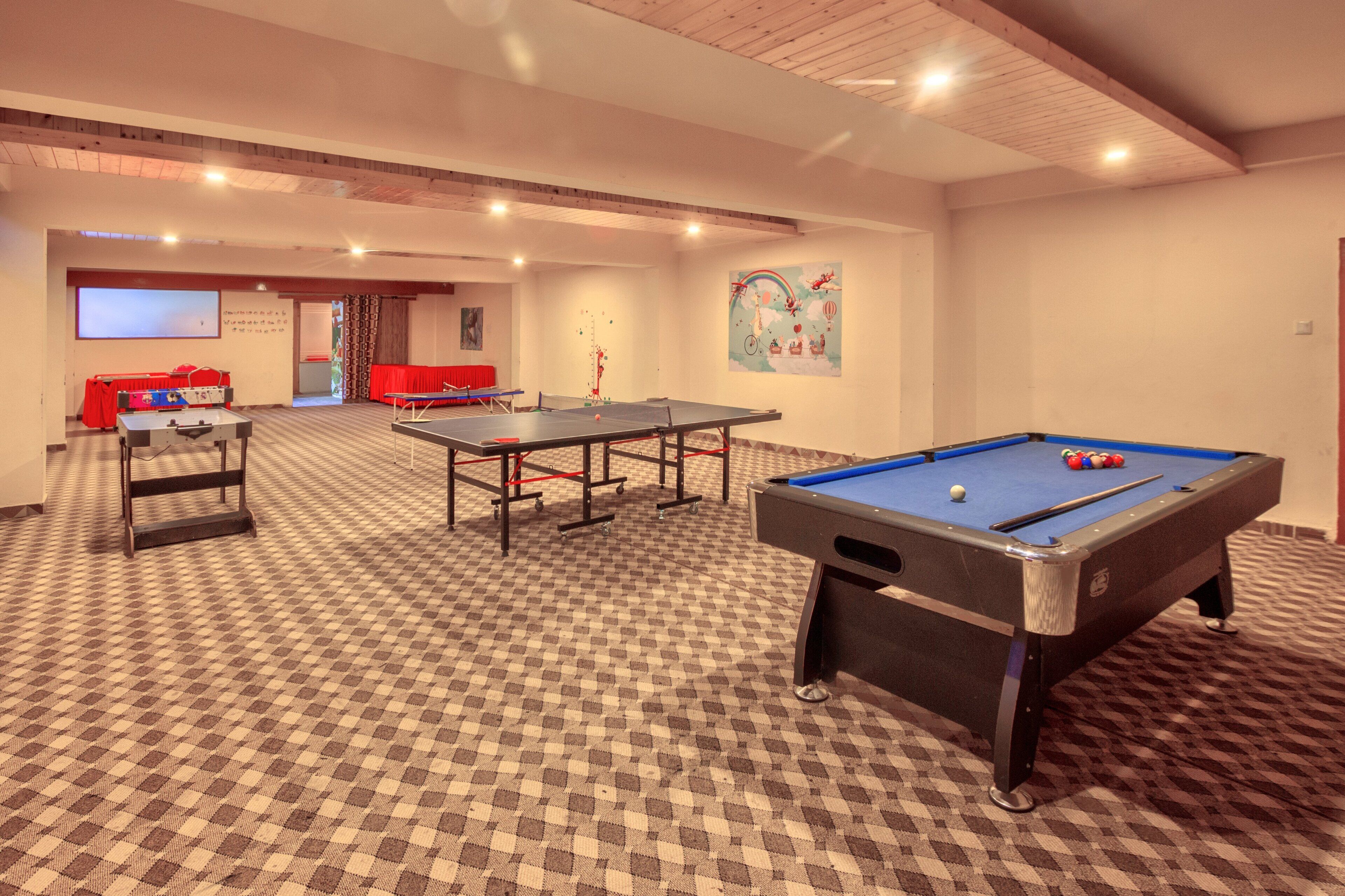 Una habitación con mesa de billar, mesa de futbolín y una pantalla de proyección.