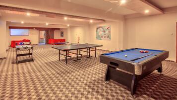 Una habitación con mesa de billar, mesa de futbolín y una pantalla de proyección.