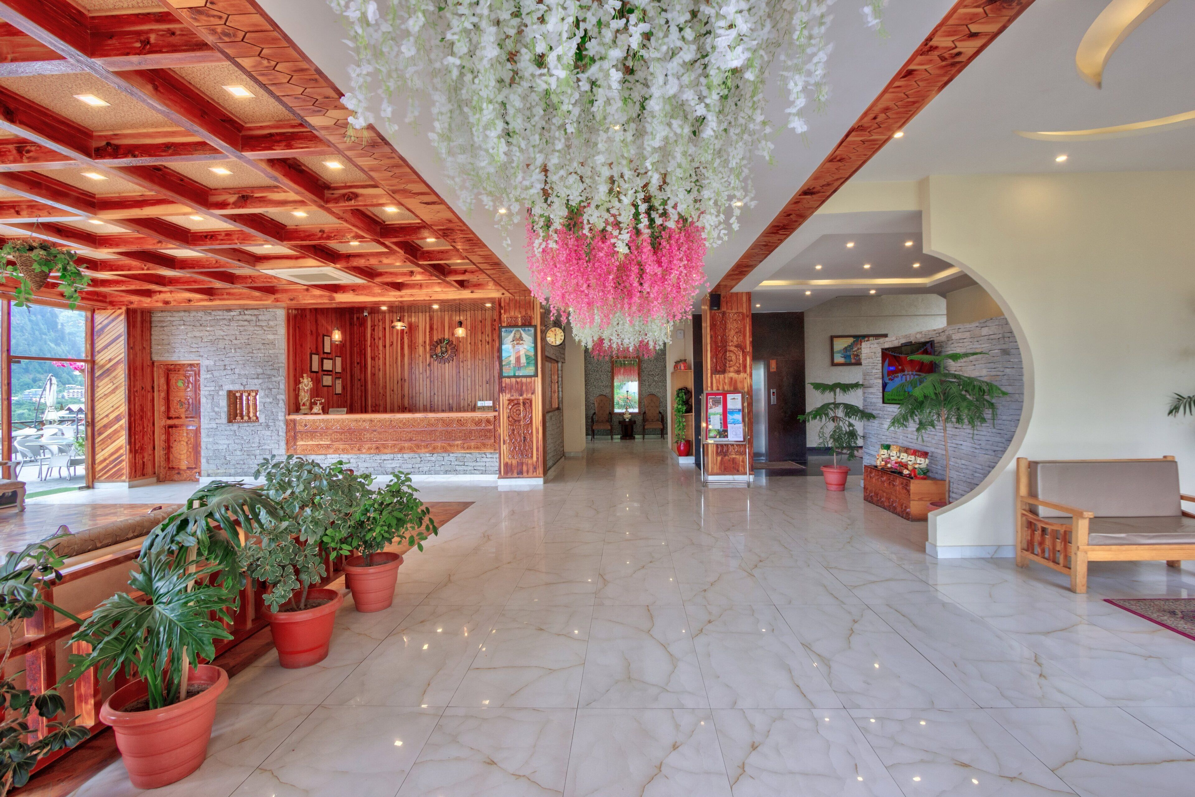 A spacious lobby with a wooden reception desk, potted plants, and hanging floral arrangements.