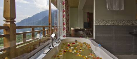 A bathroom with a bathtub filled with flower petals, a wooden balcony railing, and a view of mountains.