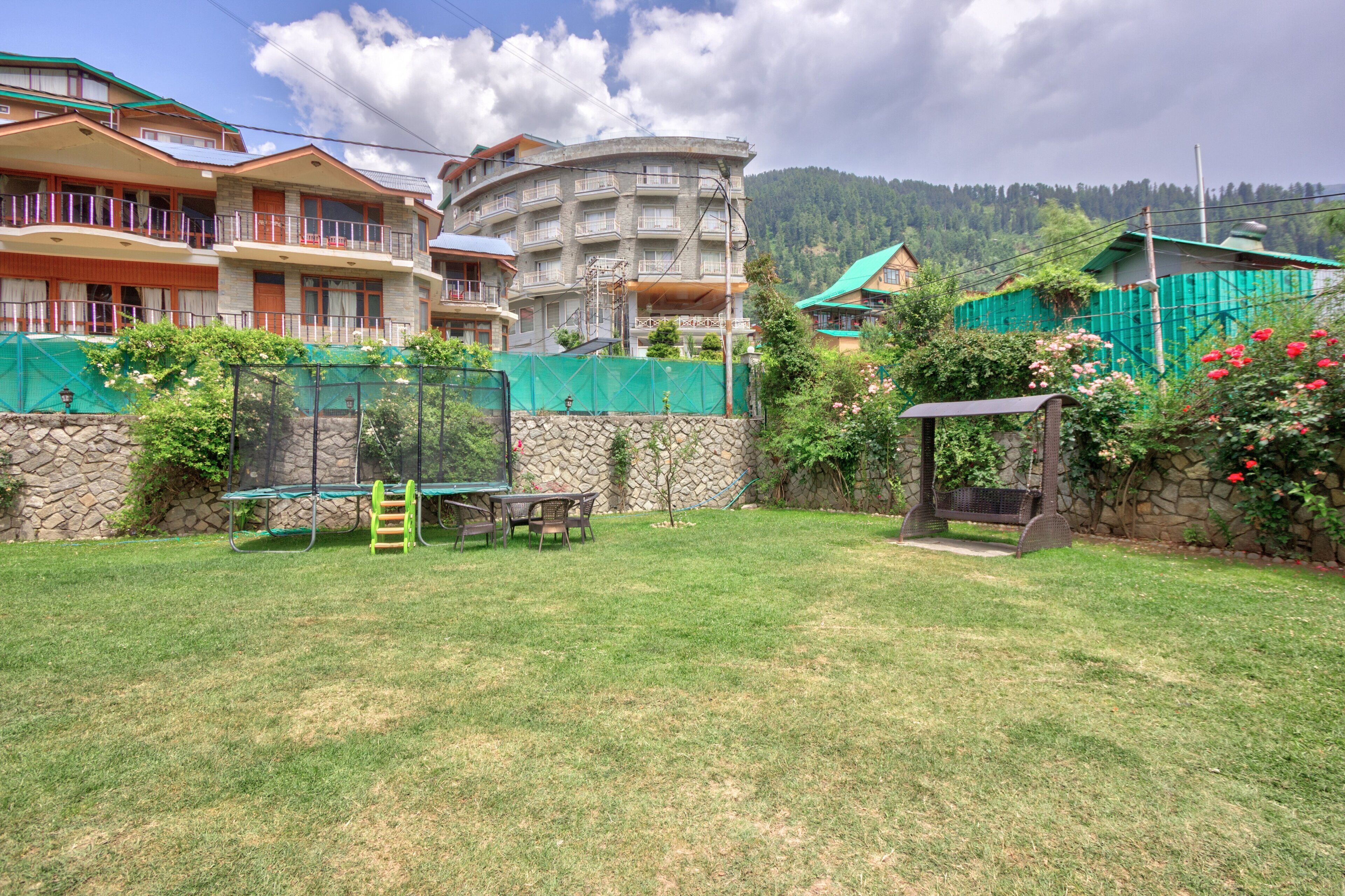 A residential area with a stone wall, a green fence, and a playground with a table and chairs.