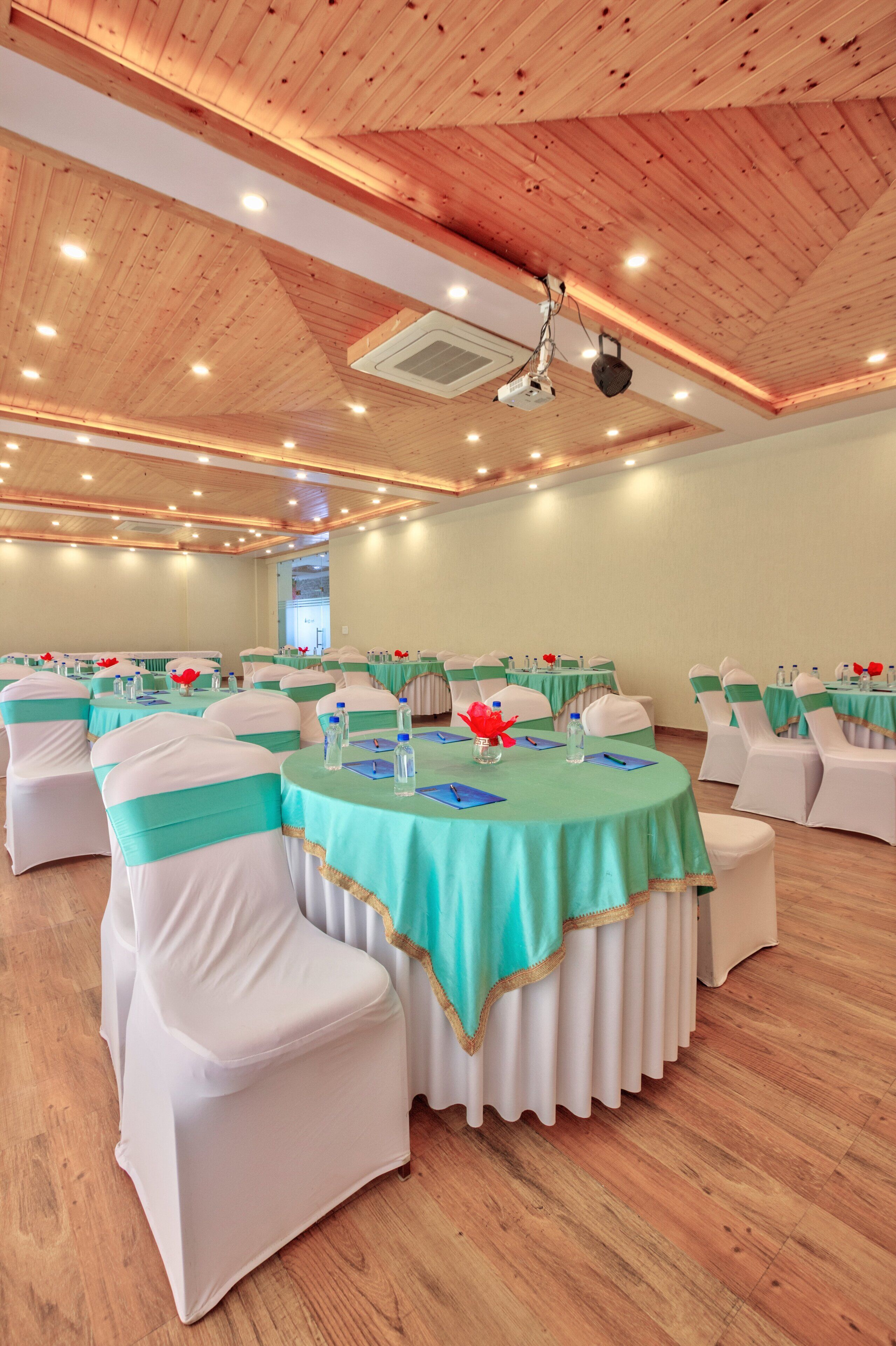 A conference room with round tables, white chairs, and teal tablecloths.