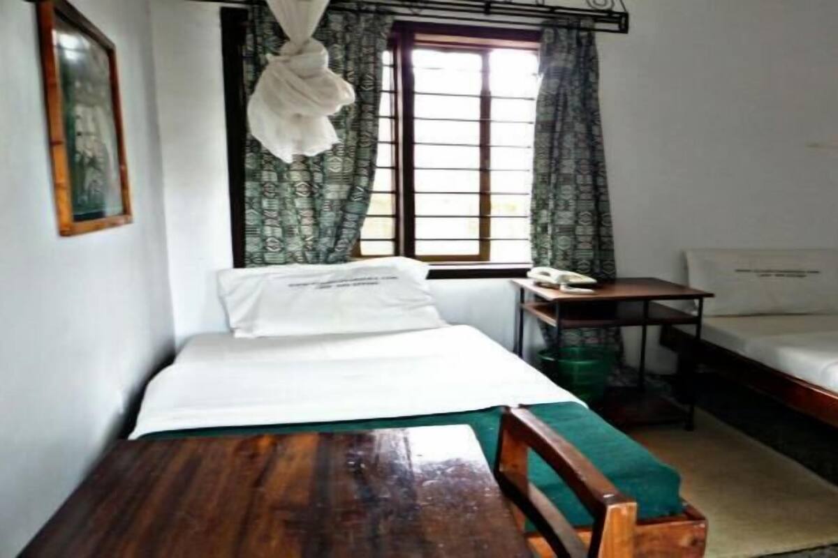 A small, simple room with two beds, a wooden table, and a window with curtains.