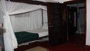 Quarto com cama coberta por um dossel branco, porta de madeira e piso vermelho.