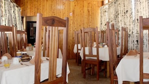 Uma área de refeições com cadeiras e mesas de madeira, cada conjunto com toalha e guardanapos brancos.