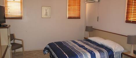 Une chambre à coucher comprenant un lit, un bureau, une chaise et un climatiseur fixé au mur.