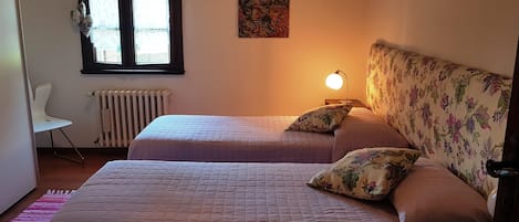 A bedroom with two beds, a radiator, a chair, and a window with curtains.