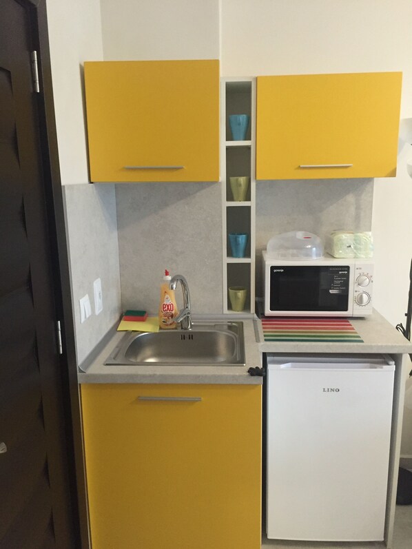 Una cocina compacta con armarios amarillos, un lavamanos de acero inoxidable, un microondas y un refrigerador pequeño.