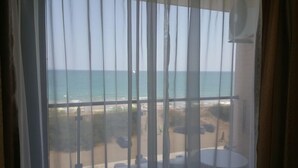 A window with vertical blinds, a view of the sea, and a beach with umbrellas. - Apart Hotel Iglika (Pomorie)
