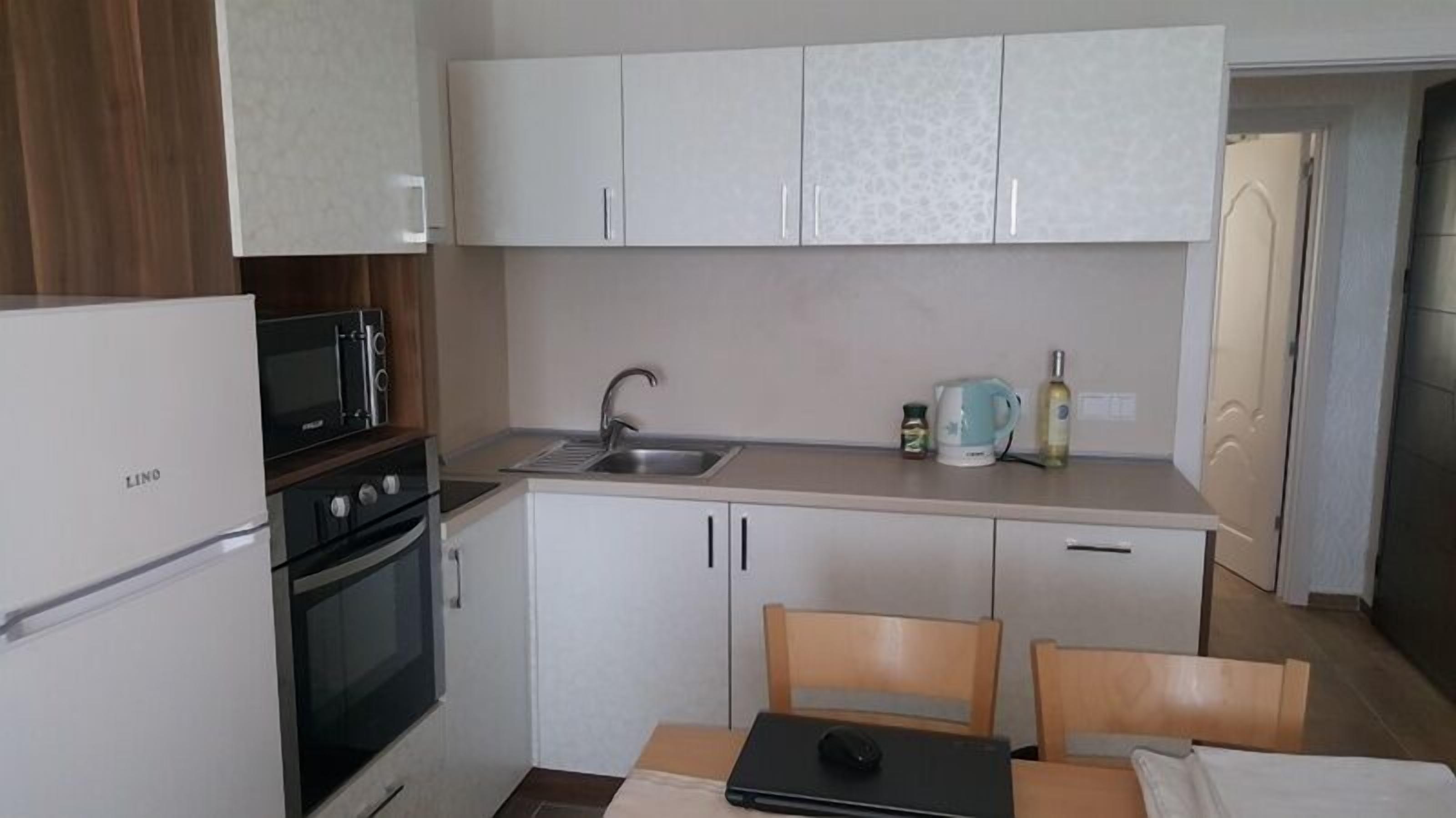 Eine kompakte Küche mit Kühlschrank, Herd, Mikrowelle, Spüle und einer kleinen Essecke mit Tisch und Stühlen.