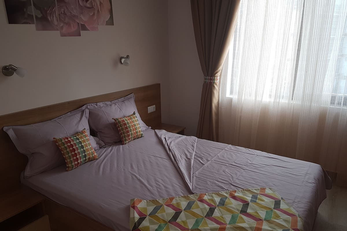 A neatly made bed with a patterned pillow, a wooden headboard, and a wall-mounted light fixture.