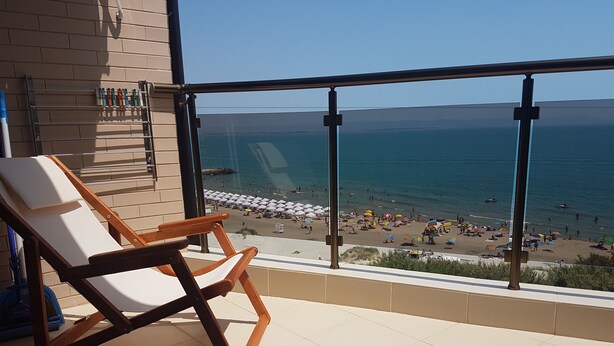 A balcony with a view of a beach, a chair, and a towel rack. - Apart Hotel Iglika (Pomorie)