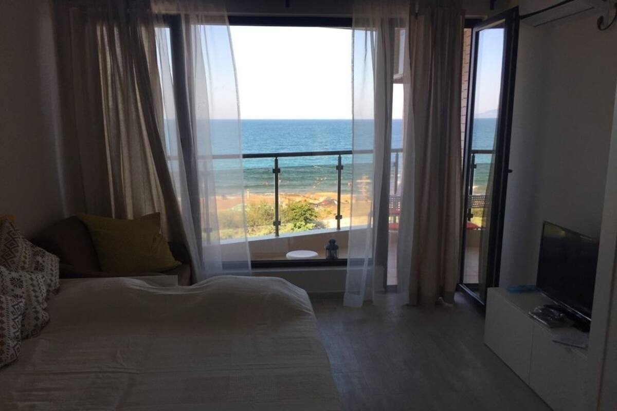 A bedroom with a bed, a TV, and a balcony with a view of the sea.