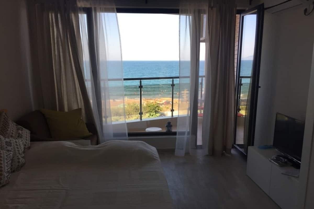 A bedroom with a bed, a TV, and a balcony with a view of the sea.