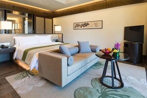 Une chambre d’hôtel avec un lit, un canapé, une petite table avec des fruits, une télévision et un miroir.