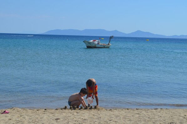 Una playa con dos niños jugando en la arena, un bote en el agua y montañas al fondo.