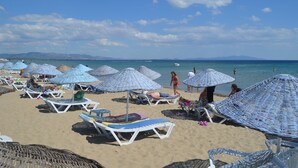 A beach with sun loungers and umbrellas, a clear sky, and calm sea. - Yasmin Hotel (Ayvalik)