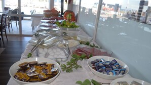 A buffet table with various food items and a view of the outside. - Yasmin Hotel (Ayvalik)