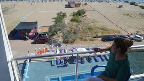A balcony with a pool, beach view, lounge chairs, and umbrellas. - Yasmin Hotel (Ayvalik)