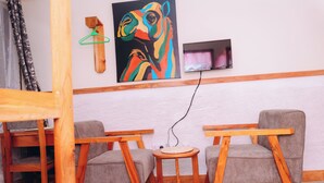 A room with two grey sofas, a wooden table, a painting on the wall, and a TV mounted above a small table. - Arusha Giraffe Lodge (Arusha)