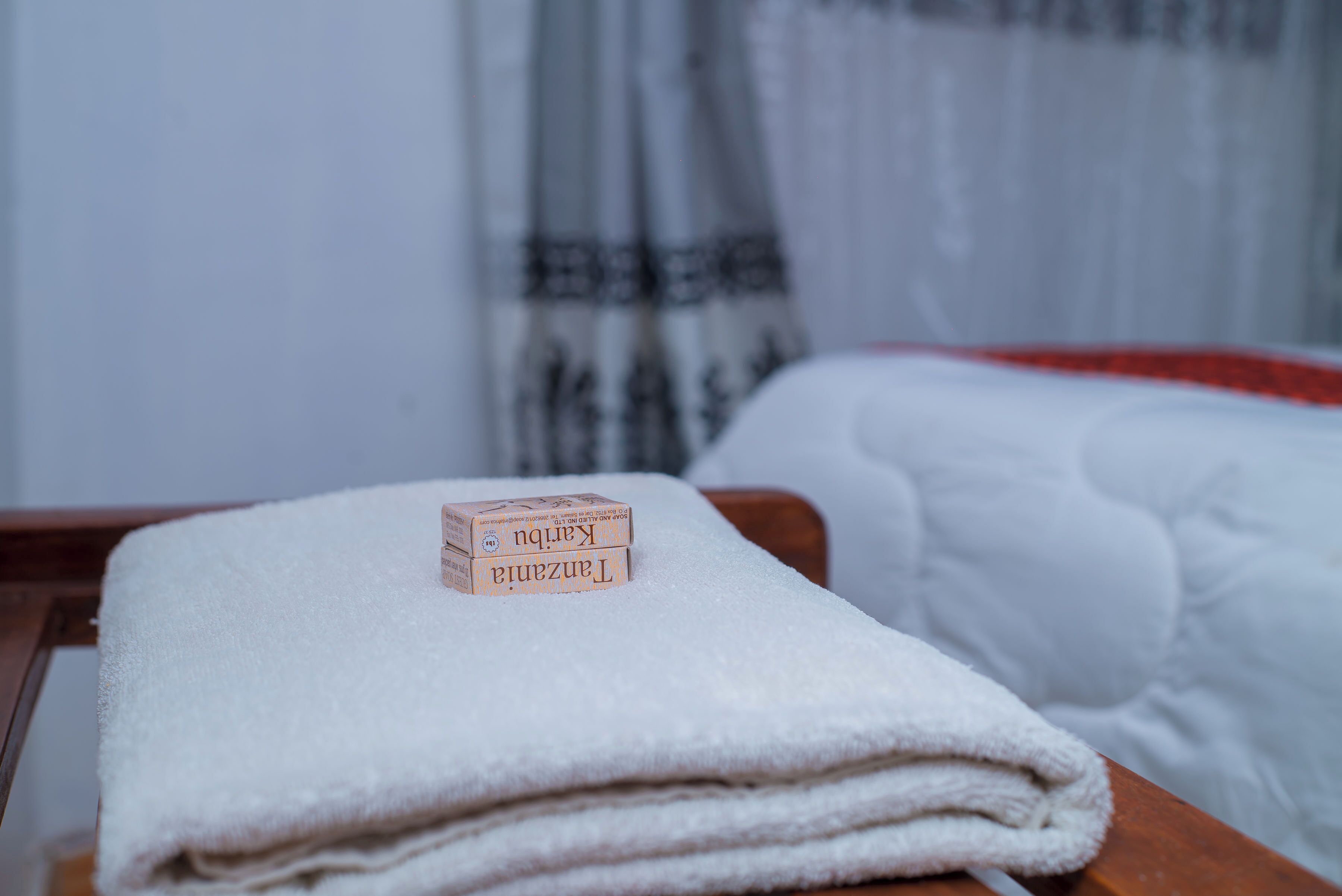 A neatly folded white towel on a wooden surface with a small wooden block labeled 'TANZANIA' on top.