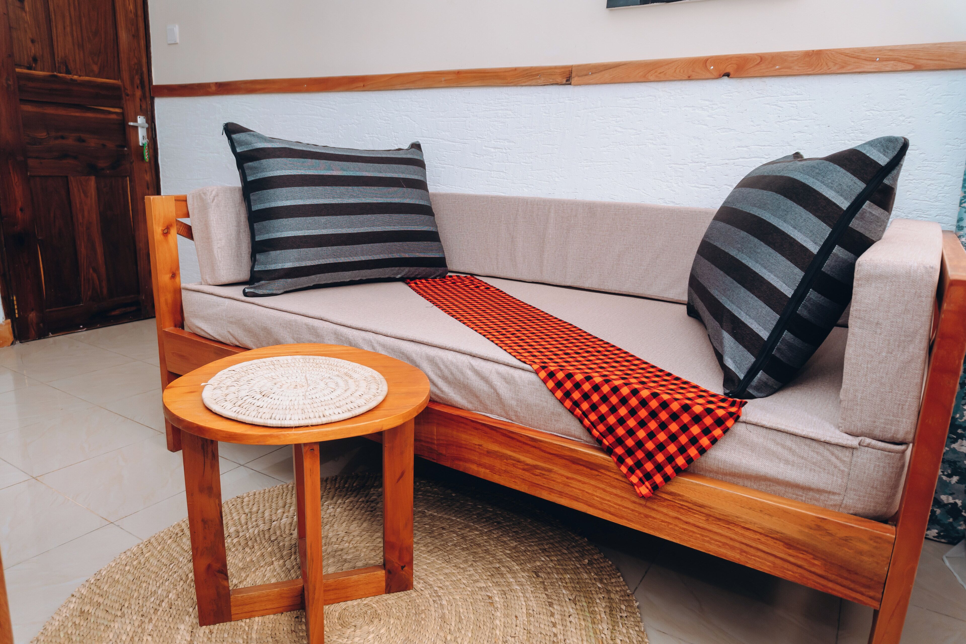 Un sofá de madera con almohadones a rayas, una mesa tejida y un plaid de cuadros.