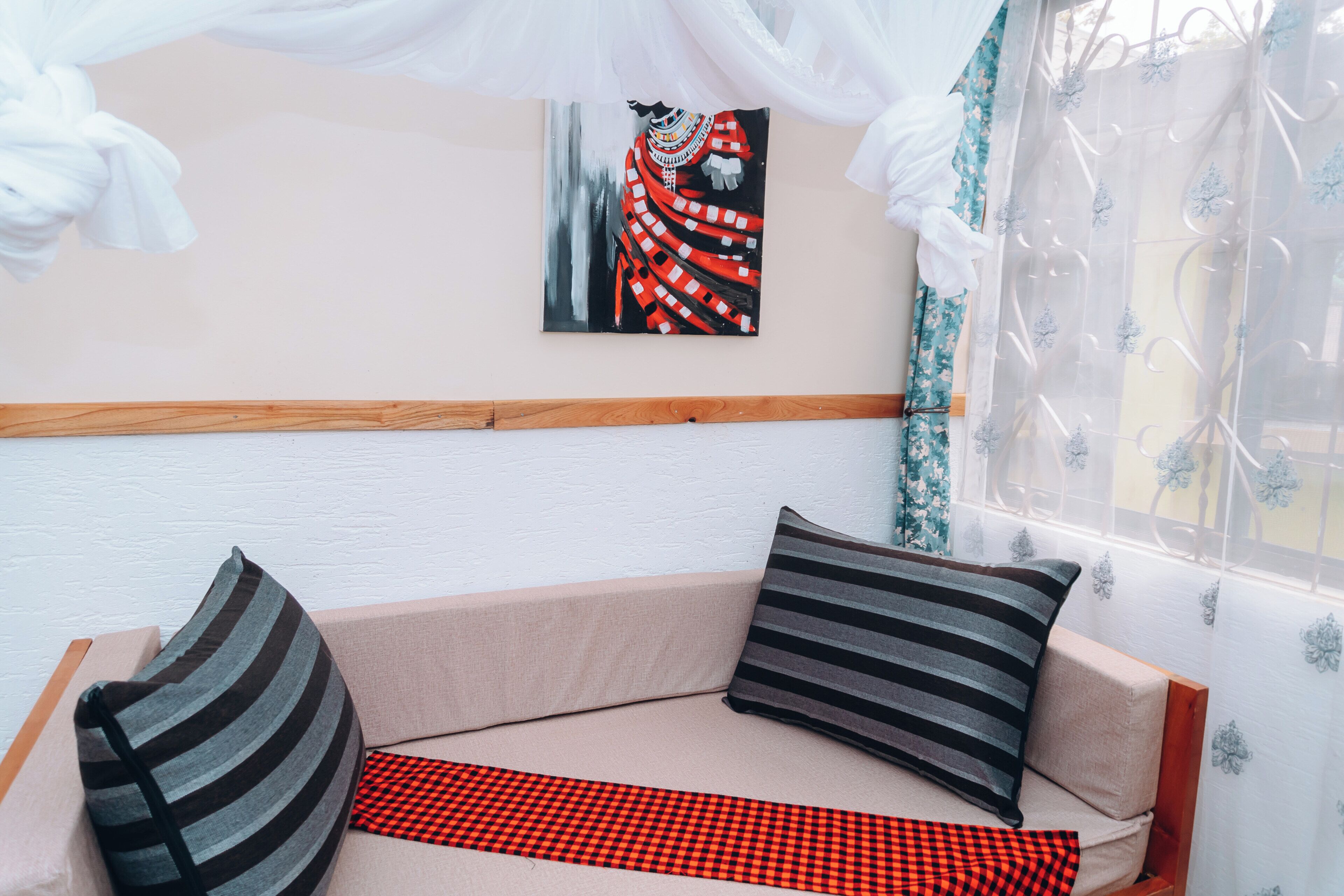 Una habitación con una zona de estar acolchada, un cuadro en la pared y una ventana con cortinas de gasa.