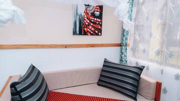 Una habitación con una zona de estar acolchada, un cuadro en la pared y una ventana con cortinas de gasa.
