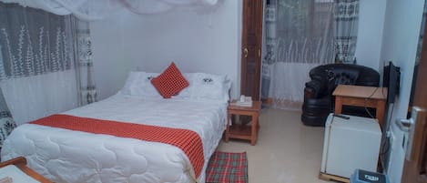 A bedroom with a bed, bedside table, chair, and a small desk with a computer.