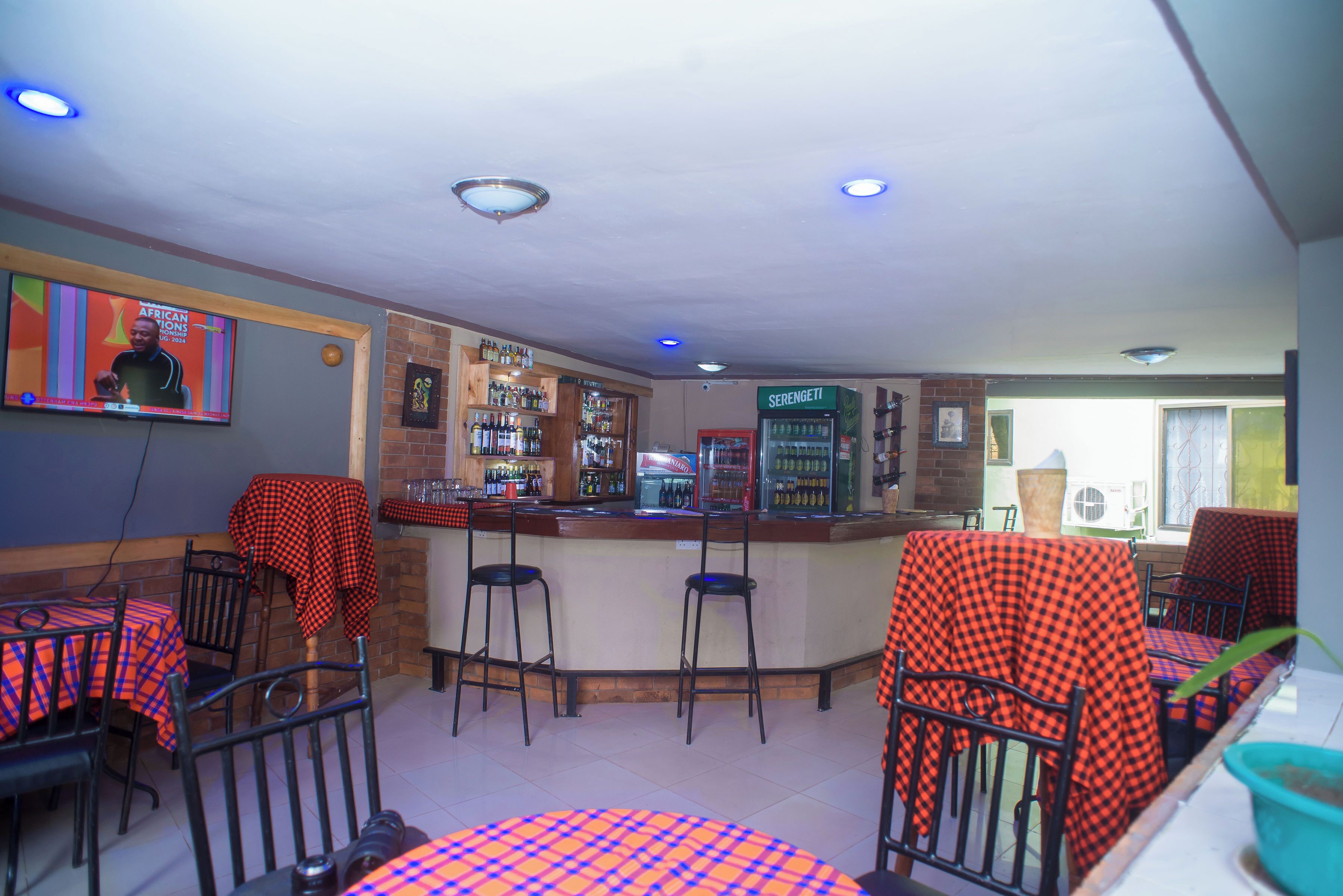 A bar area with a counter, stools, and a television screen displaying a sports event.