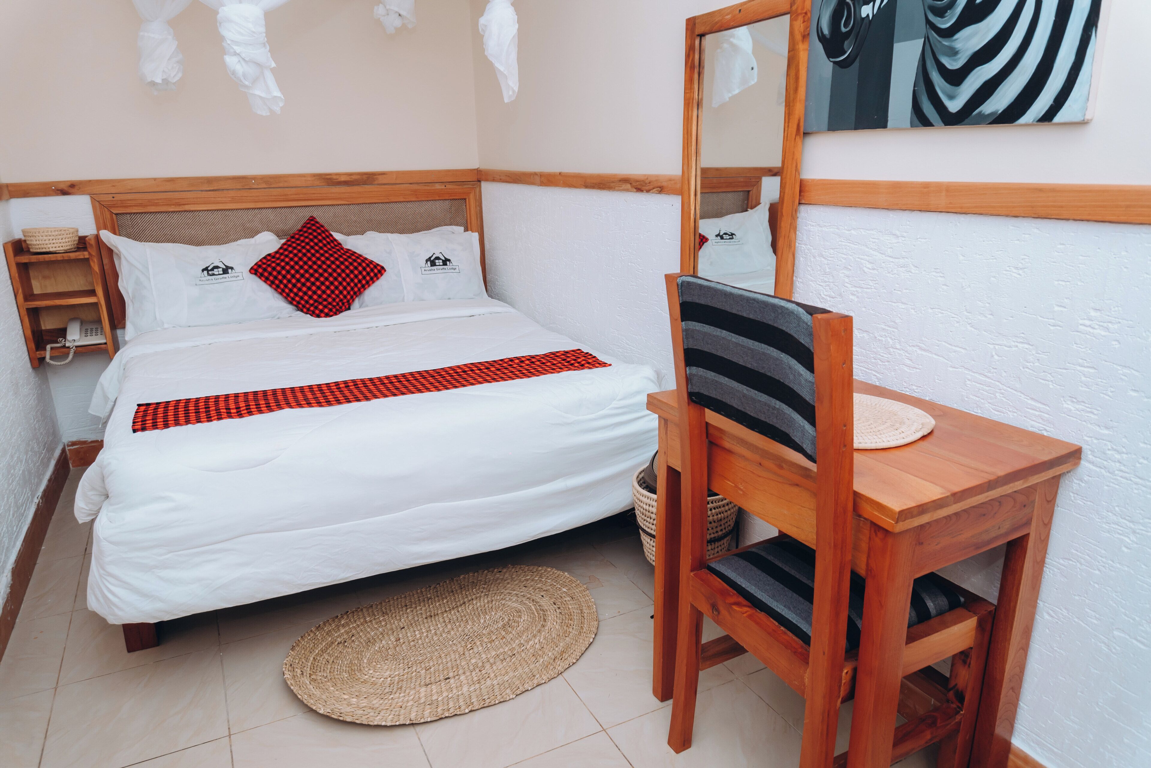 Ein ordentlich eingerichtetes Schlafzimmer mit einem Bett, einem Holzstuhl, einem kleinen Tisch und einem wandmontierten Spiegel.