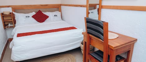 A neatly arranged bedroom with a bed, a wooden chair, a small table, and a wall-mounted mirror.
