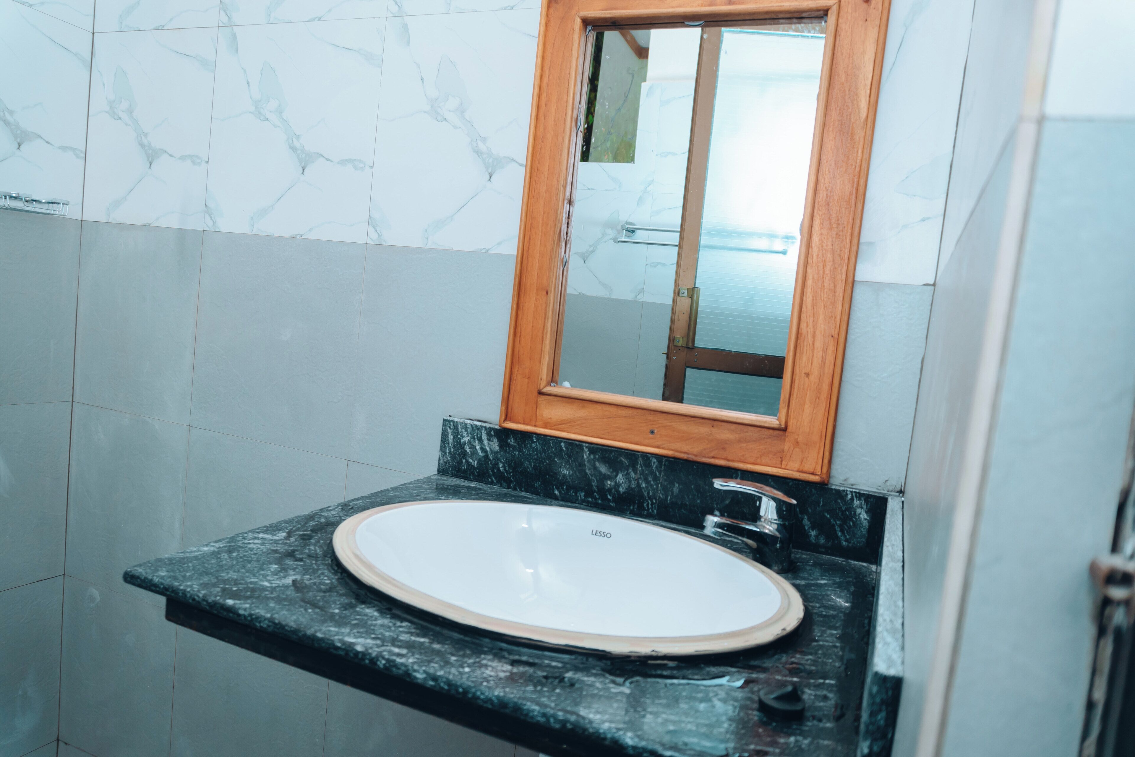 A bathroom with a marble wall, a wooden-framed mirror, and a white sink on a black countertop.