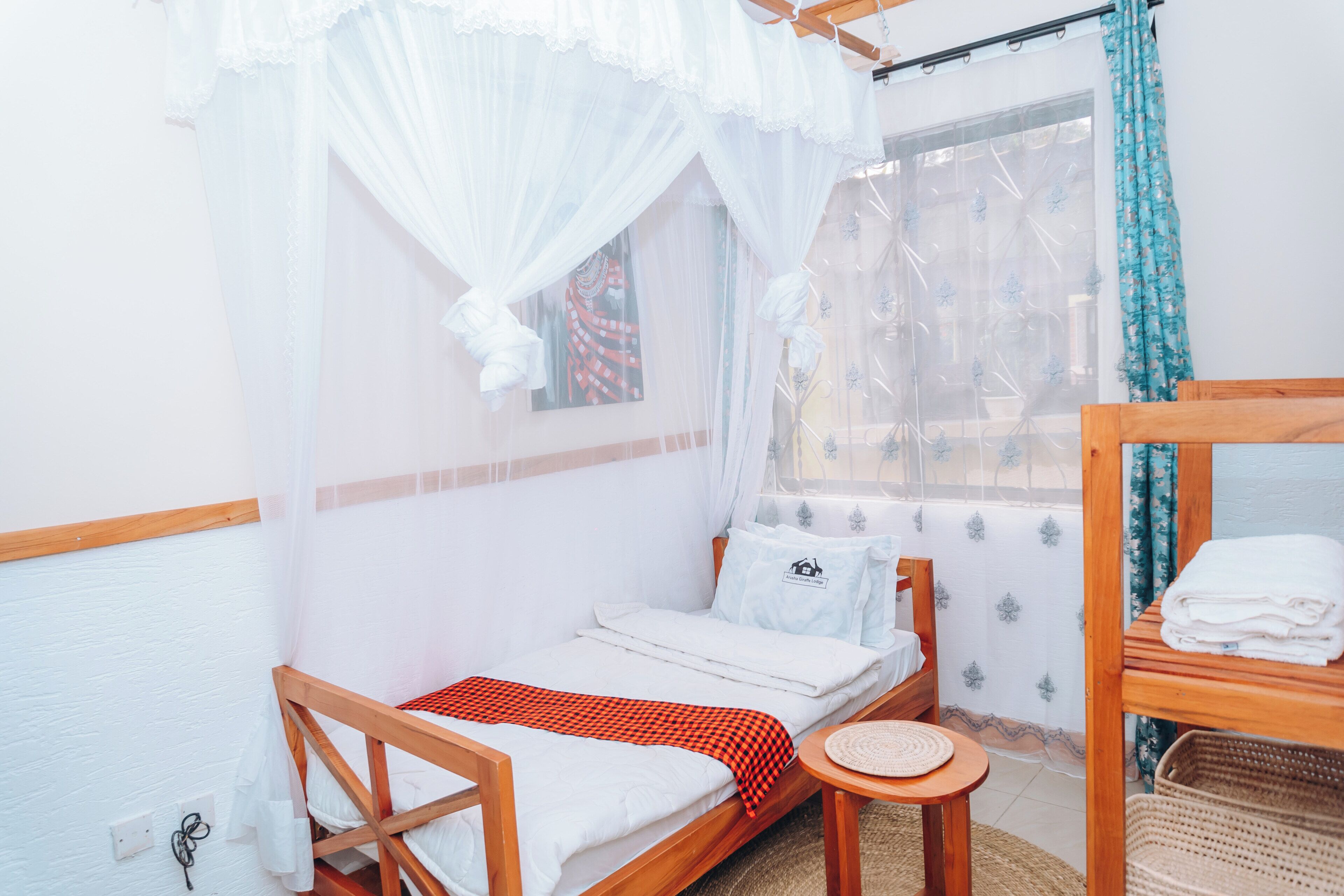 A single bed with a red checkered blanket, a small round table, and a window with curtains.