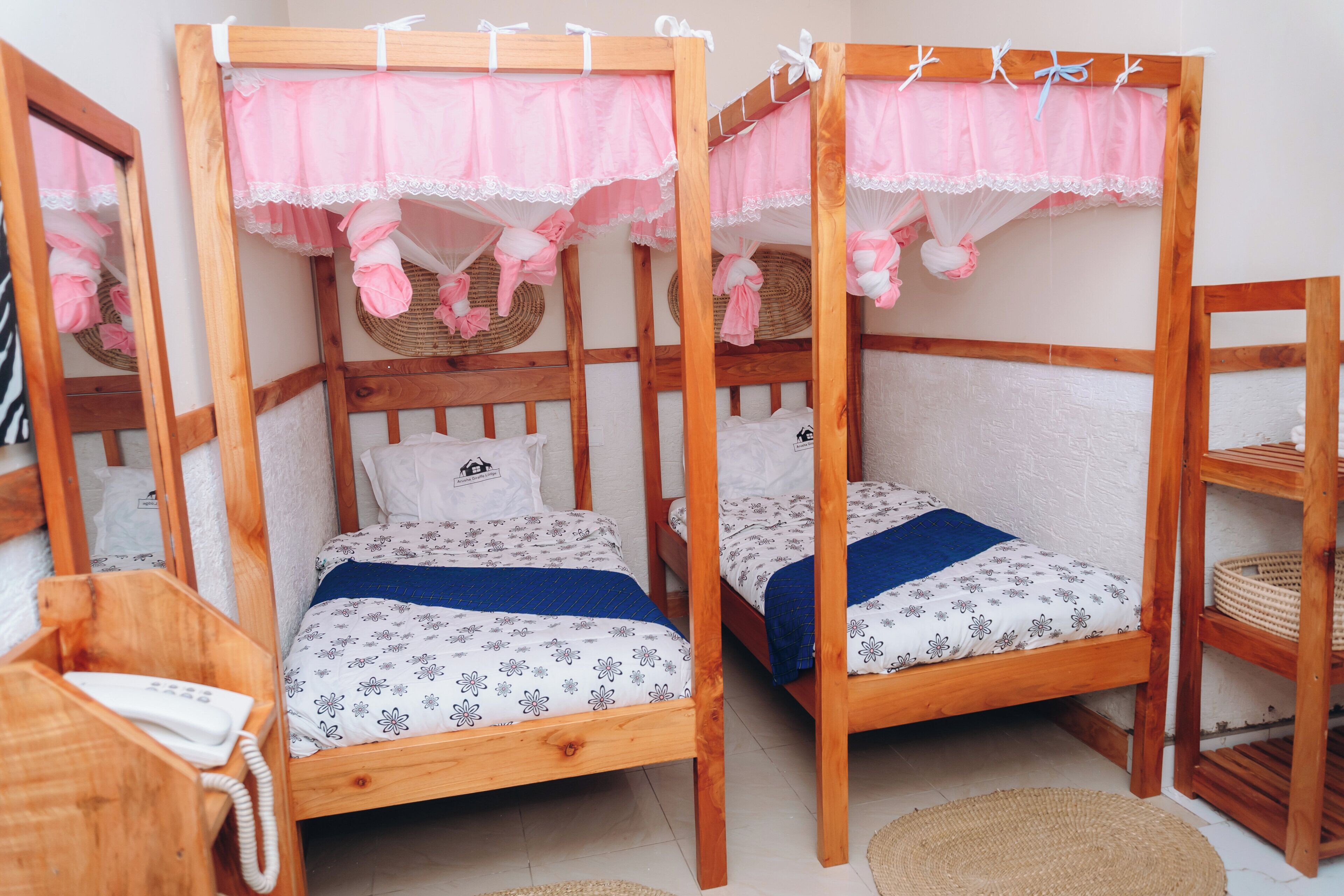 A room with two wooden bunk beds with pink canopies, white bedding with floral patterns, and a small wooden chair.