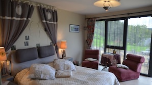 Un dormitorio con una cama grande, un sillón rojo, una mesita pequeña y vistas al exterior a través de un ventanal amplio.
