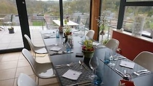 Un comedor con una mesa dispuesta para dos personas, sillas, un florero con flores y vistas al exterior.