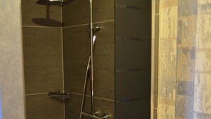Zona de ducha con mampara de vidrio, cabezal de ducha de mano y grifo empotrado.