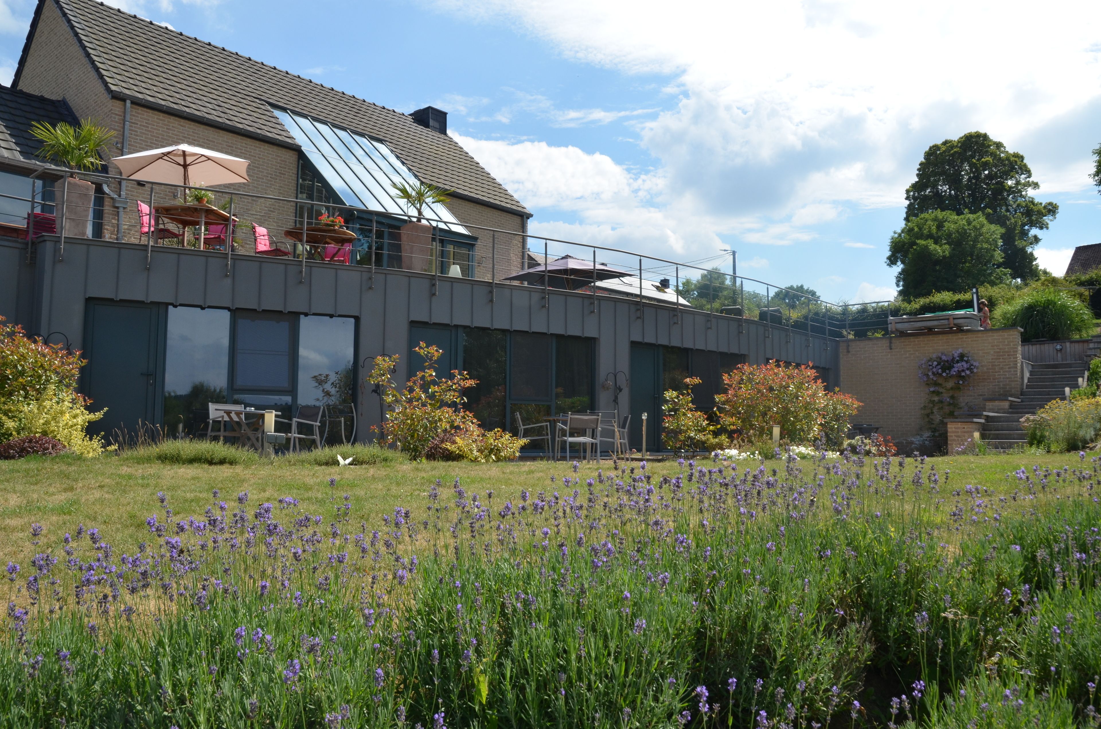 A modern building with a flat roof, large windows, and a balcony with outdoor seating.