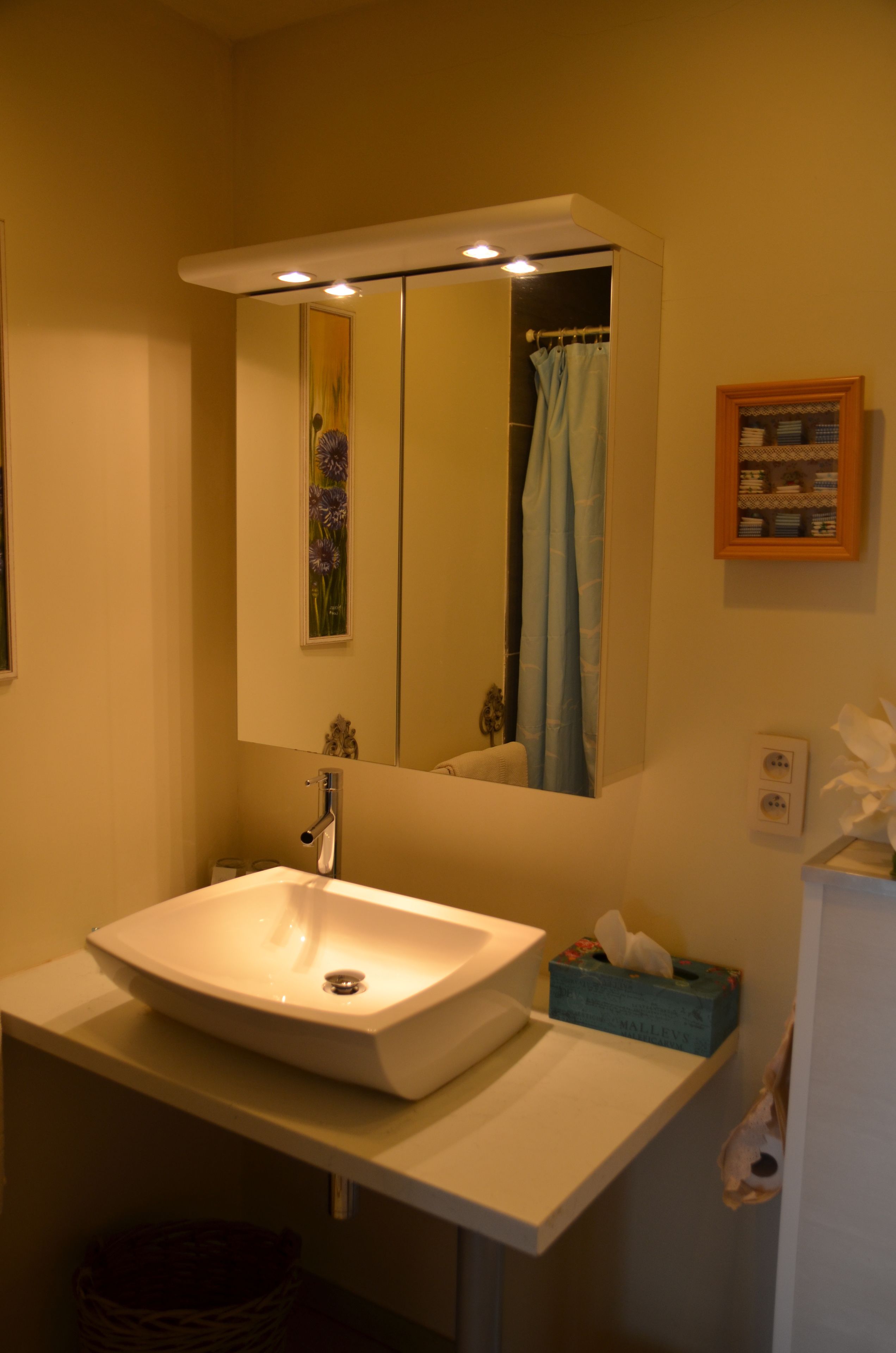 A bathroom with a white sink, a mirror above it, a blue shower curtain, and a small framed picture on the wall.