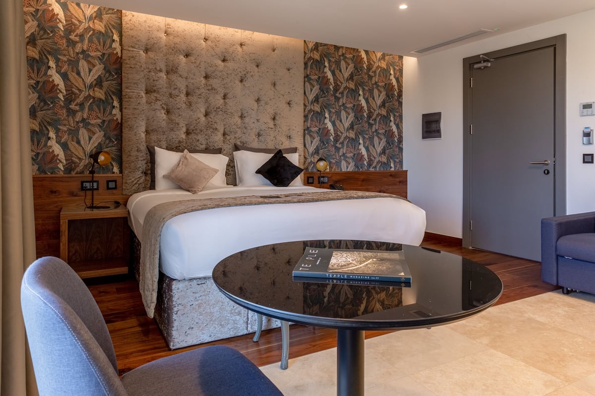 Quarto de hotel com uma cama grande, uma mesa redonda e uma cadeira azul.