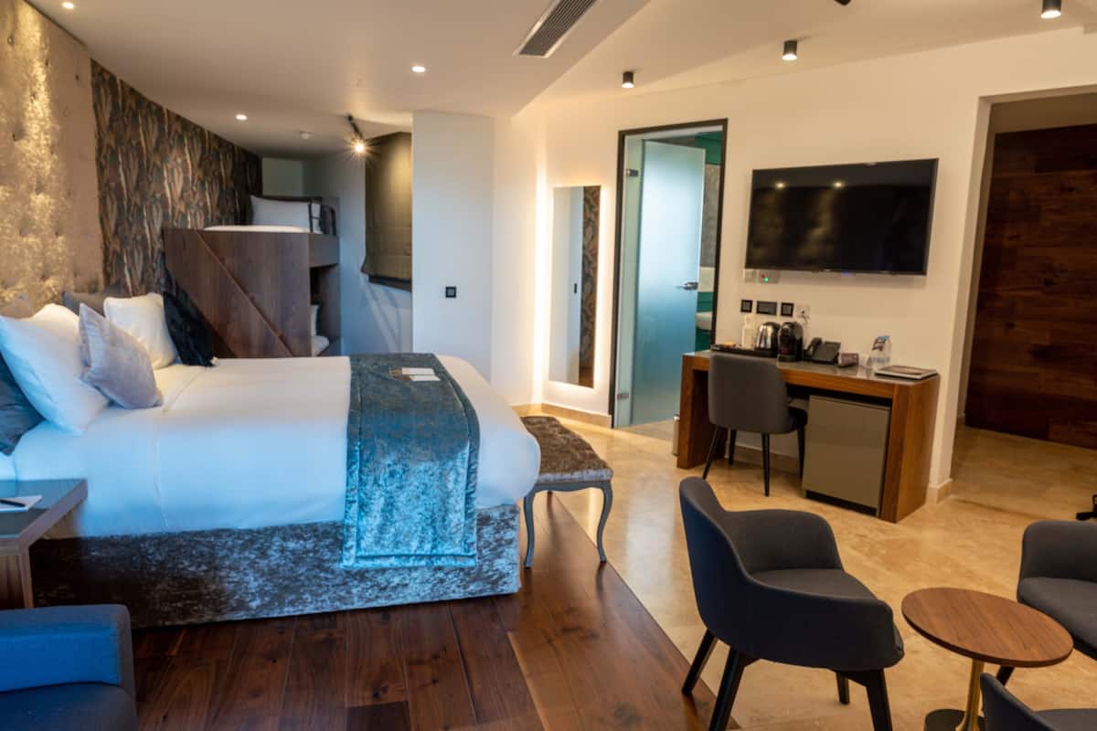 Quarto de hotel moderno com uma cama grande, uma escrivaninha, uma cadeira e uma televisão.