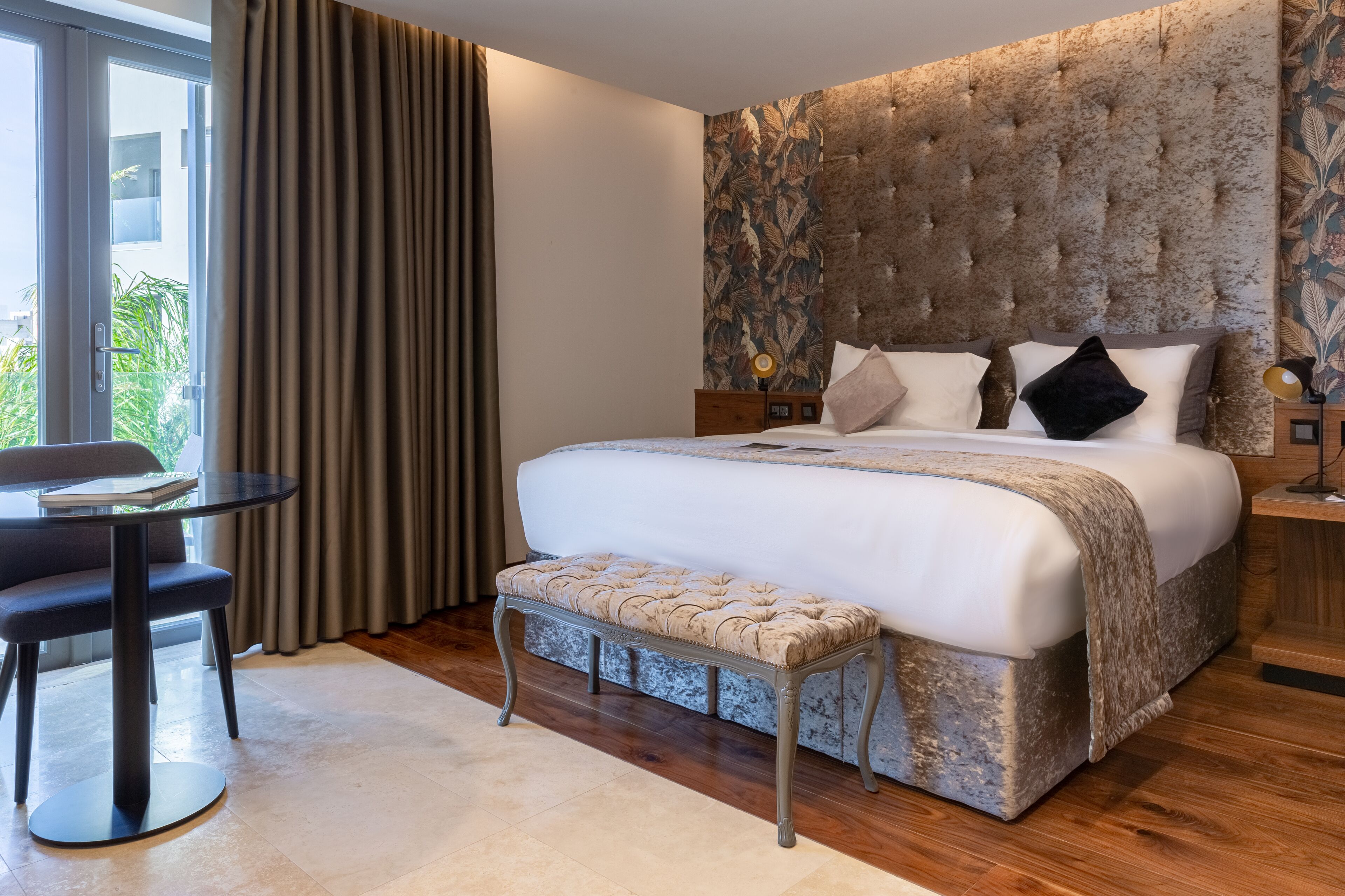 A modern hotel room with a large bed, a small table, and a bench.