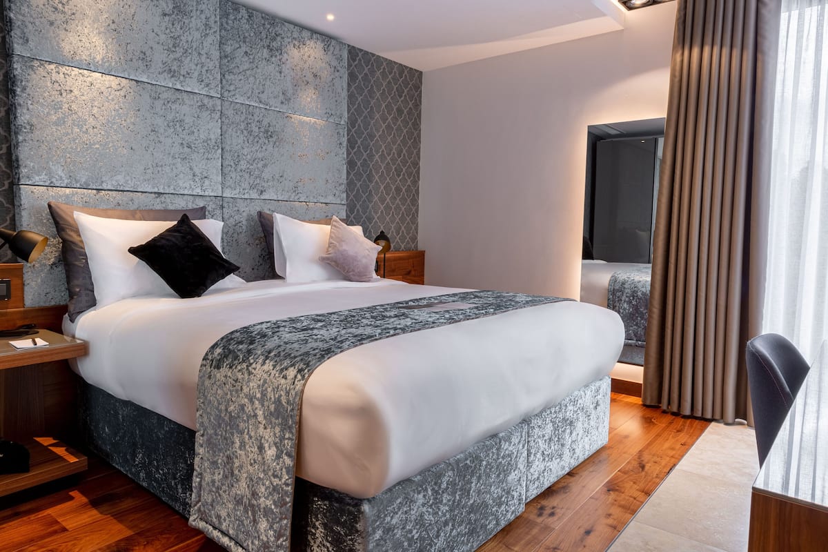 Quarto de hotel moderno com uma cama grande, piso de madeira e vista para a cidade.