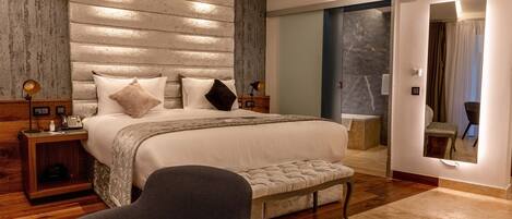 Un dormitorio moderno con una cama grande, cabecera de madera, lámparas de noche, un banco y un espejo.