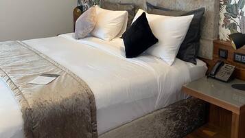 A neatly made bed with a white comforter and pillows, a wooden nightstand with a telephone, and a wall with a floral pattern.