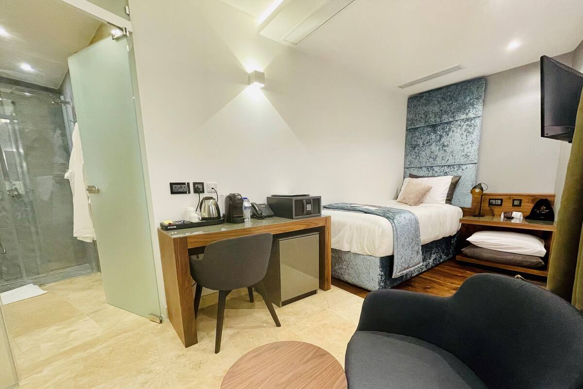 Quarto de hotel com cama, escrivaninha, cadeira e uma pequena mesa.