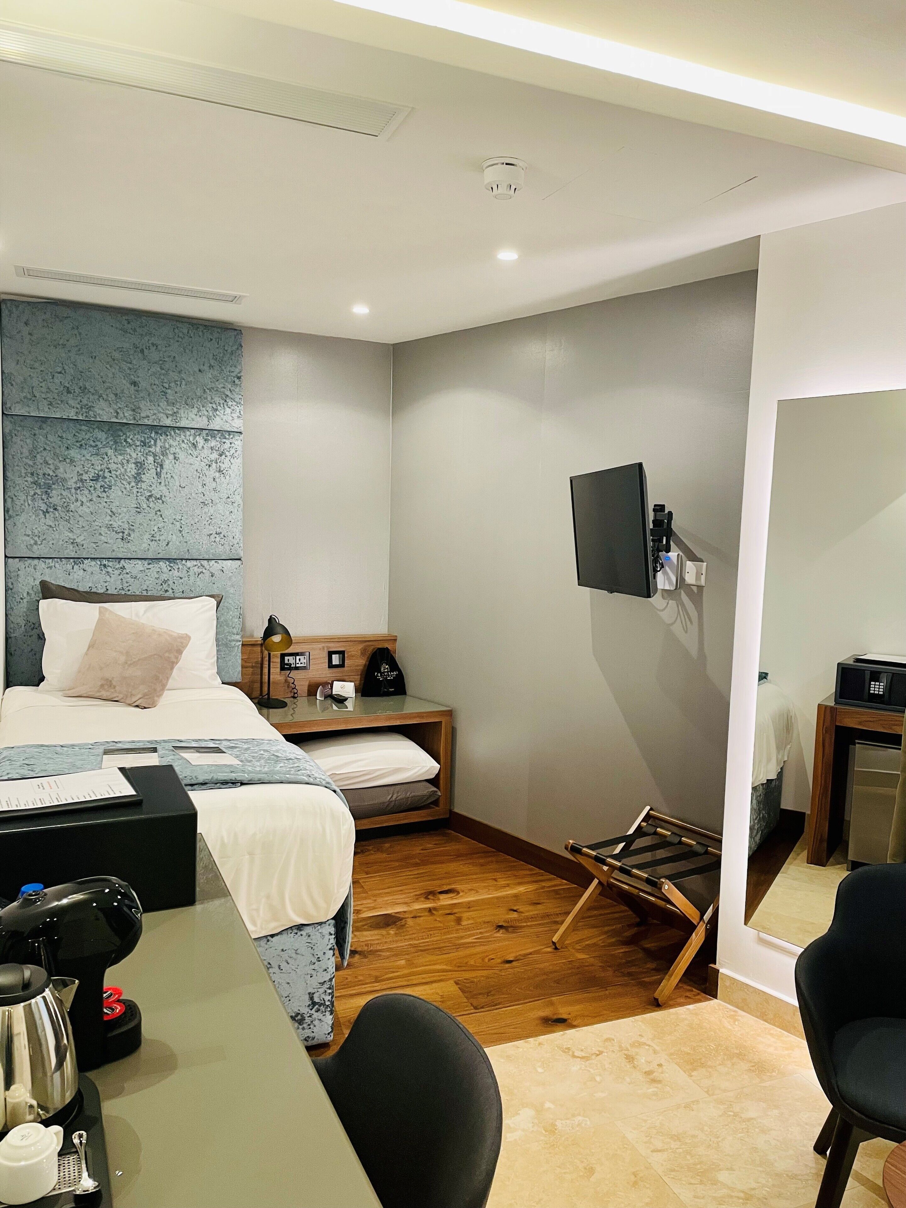 A modern hotel room with a bed, bedside table, desk, chair, and a television mounted on the wall.